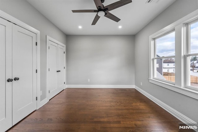 unfurnished bedroom featuring ceiling fan, dark hardwood / wood-style flooring, multiple windows, and two closets