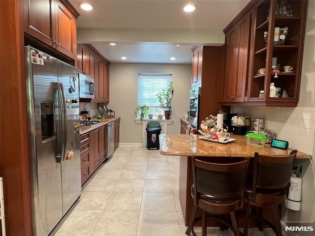 kitchen with kitchen peninsula, appliances with stainless steel finishes, decorative backsplash, light stone countertops, and a kitchen breakfast bar