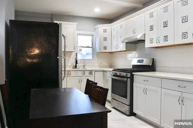 kitchen with decorative backsplash, black refrigerator, white cabinetry, and stainless steel range with gas stovetop