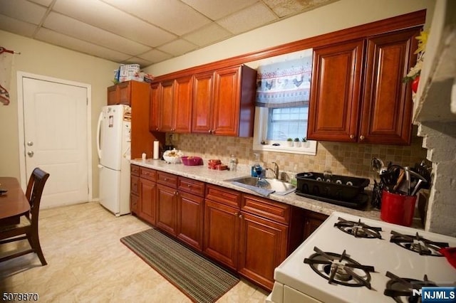 kitchen with sink, white appliances, backsplash, and a drop ceiling