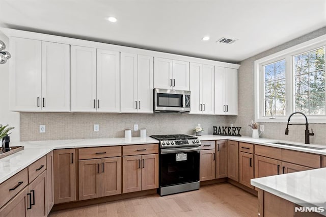 kitchen with white cabinetry, sink, light hardwood / wood-style floors, decorative backsplash, and appliances with stainless steel finishes