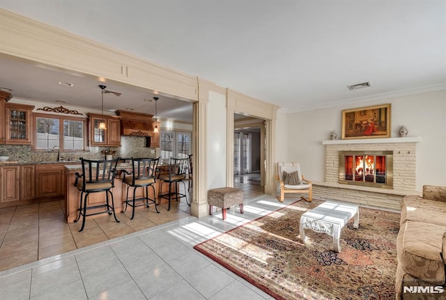 living room with sink, a stone fireplace, crown molding, and light tile patterned floors