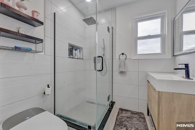 bathroom with toilet, an enclosed shower, tile walls, and vanity