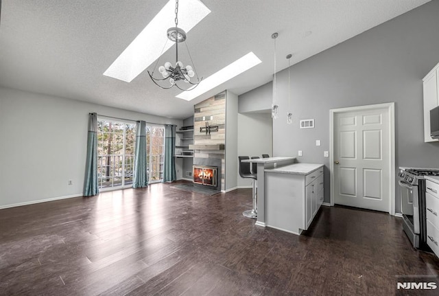 kitchen featuring lofted ceiling with skylight, white cabinets, stainless steel range with gas cooktop, decorative light fixtures, and a tiled fireplace