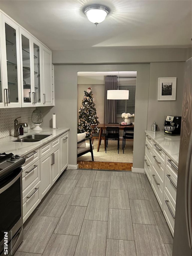 kitchen with white cabinets, light stone countertops, sink, and stainless steel stove