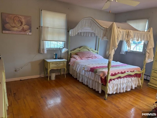 bedroom with ceiling fan, wood-type flooring, and a baseboard heating unit