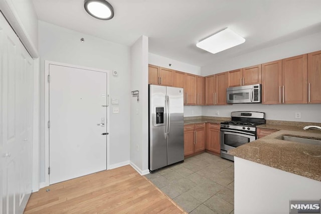 kitchen with stainless steel appliances, light hardwood / wood-style flooring, dark stone countertops, and sink