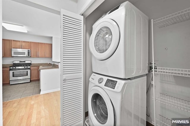 laundry room with sink, light tile patterned flooring, and stacked washer and clothes dryer