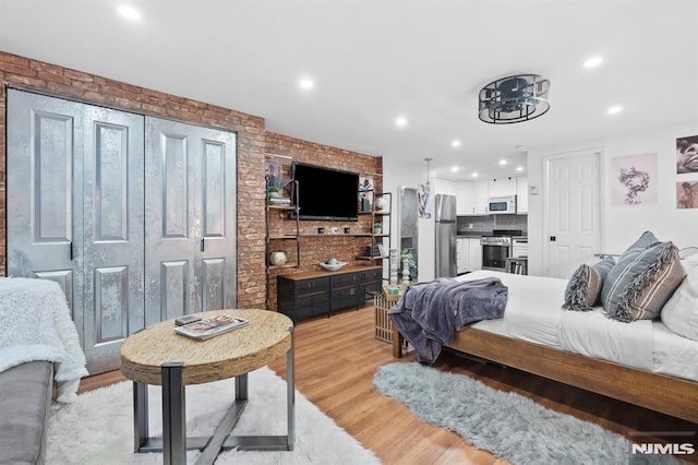 bedroom featuring stainless steel fridge, light hardwood / wood-style flooring, and brick wall