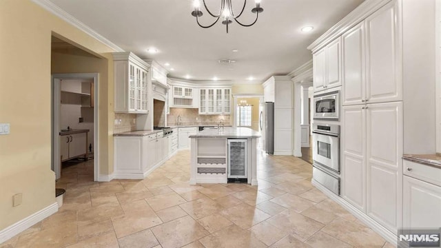 kitchen with appliances with stainless steel finishes, beverage cooler, a chandelier, white cabinetry, and an island with sink