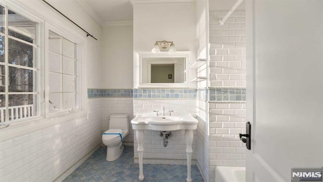 bathroom with a bath, tile patterned floors, crown molding, toilet, and tile walls