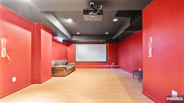 cinema with light wood-type flooring and a raised ceiling