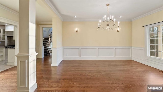 unfurnished dining area featuring decorative columns, hardwood / wood-style flooring, ornamental molding, and a notable chandelier