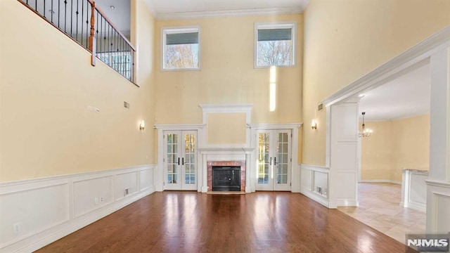 unfurnished living room with french doors, light hardwood / wood-style floors, a high ceiling, and an inviting chandelier