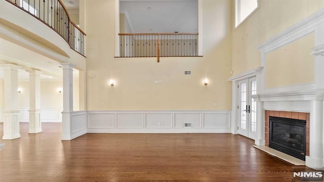 unfurnished living room featuring hardwood / wood-style floors, a towering ceiling, a fireplace, and ornate columns