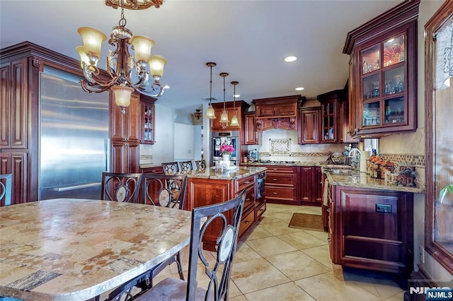 kitchen with hanging light fixtures, appliances with stainless steel finishes, a kitchen island, light stone countertops, and decorative backsplash