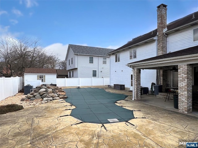 rear view of house with a shed, a covered pool, a patio, and central air condition unit