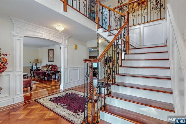 stairway with parquet floors, crown molding, decorative columns, and a towering ceiling