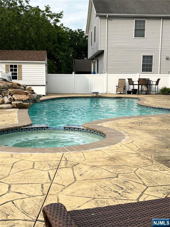 view of pool with an in ground hot tub, a patio, and an outbuilding