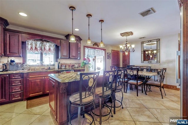 kitchen with a kitchen island, a breakfast bar area, hanging light fixtures, light tile patterned floors, and light stone countertops