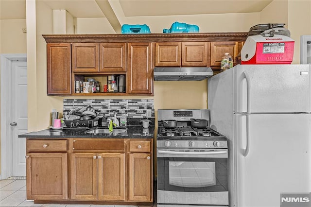 kitchen featuring decorative backsplash, sink, light tile patterned floors, white fridge, and stainless steel range with gas stovetop