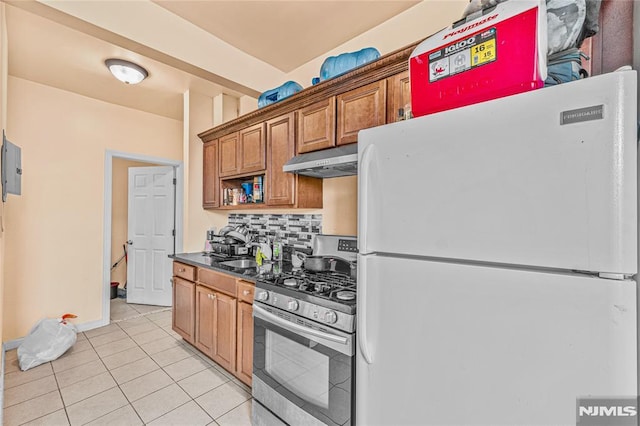 kitchen featuring decorative backsplash, gas stove, sink, light tile patterned floors, and white refrigerator