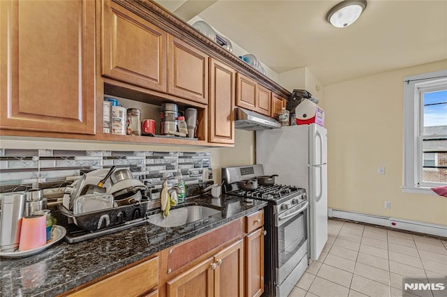 kitchen featuring dark stone counters, sink, stainless steel gas range, light tile patterned floors, and baseboard heating