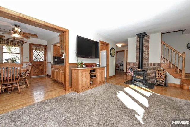 living room with a wood stove, light carpet, and ceiling fan