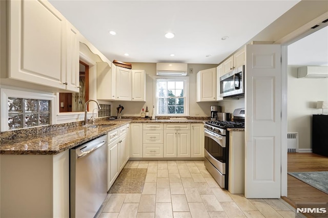 kitchen with radiator, appliances with stainless steel finishes, a wall mounted air conditioner, sink, and dark stone countertops