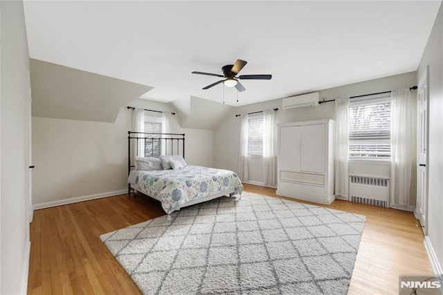 bedroom with ceiling fan, radiator heating unit, a wall mounted AC, and light wood-type flooring