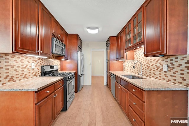 kitchen featuring sink, decorative backsplash, light wood-type flooring, light stone countertops, and appliances with stainless steel finishes