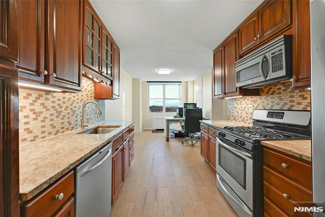 kitchen featuring light stone countertops, decorative backsplash, stainless steel appliances, sink, and light hardwood / wood-style flooring