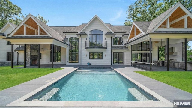 back of house with a balcony, ceiling fan, a patio area, and a lawn