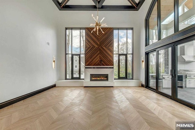 unfurnished living room with a fireplace, light parquet flooring, a chandelier, and a high ceiling