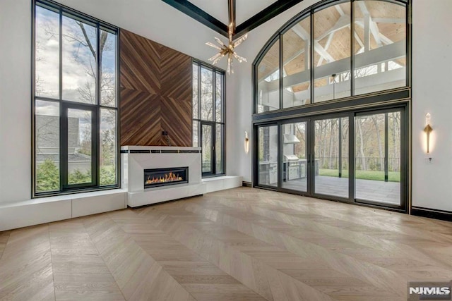 unfurnished living room with wooden walls, a towering ceiling, a notable chandelier, and parquet flooring