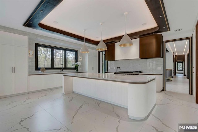 kitchen featuring a raised ceiling, an island with sink, and decorative light fixtures