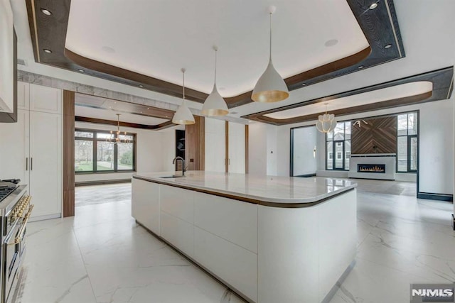 kitchen featuring white cabinets, a large island, decorative light fixtures, and a tray ceiling