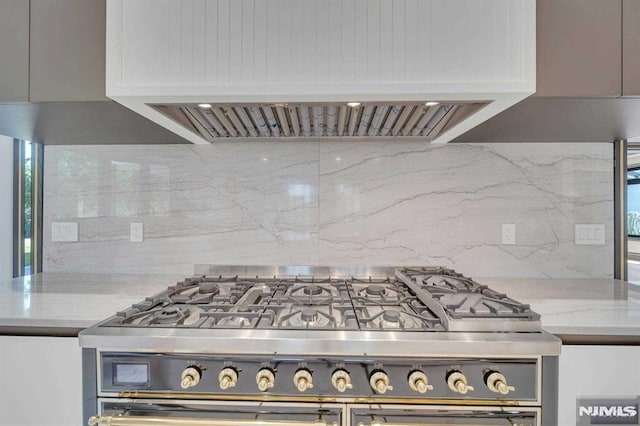 kitchen featuring light stone counters, backsplash, extractor fan, gray cabinets, and stainless steel range with gas stovetop