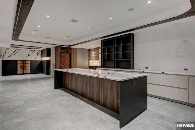 kitchen featuring dark brown cabinetry, white cabinetry, a large island, light stone counters, and a tray ceiling