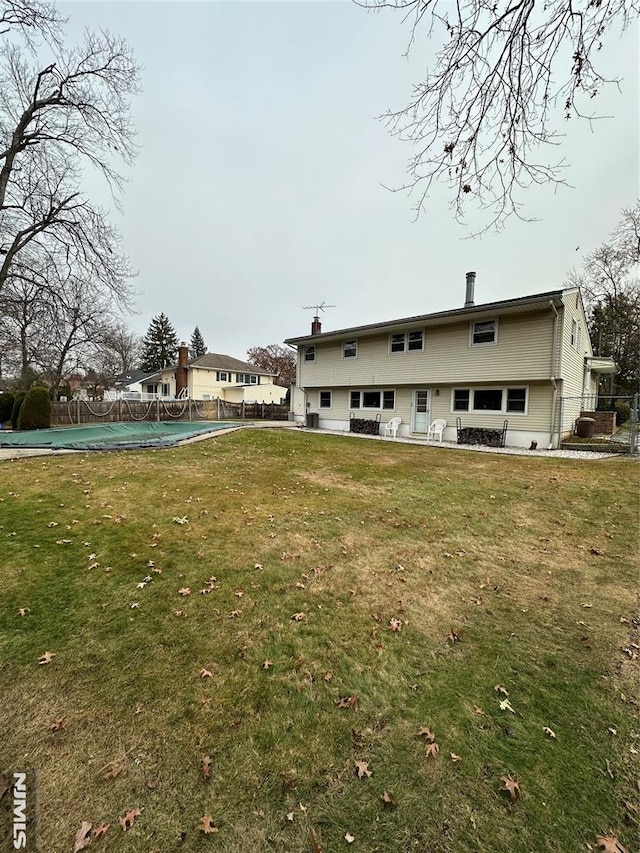 rear view of house featuring a covered pool and a lawn