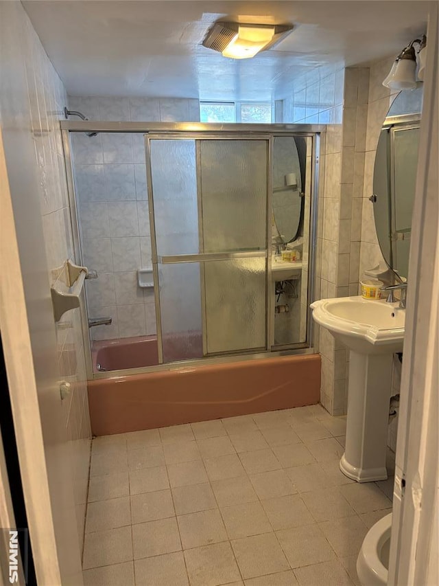 bathroom featuring tile patterned floors, toilet, combined bath / shower with glass door, and tile walls