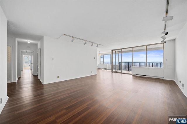 unfurnished living room with rail lighting, dark wood-style floors, and baseboards