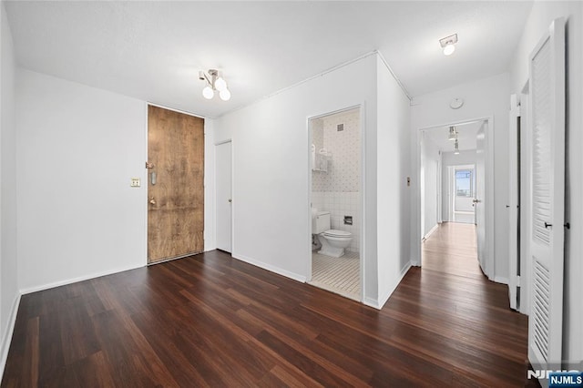 unfurnished bedroom with ensuite bath, baseboards, and wood finished floors