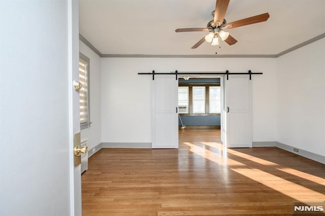 spare room featuring a barn door, ceiling fan, light wood-type flooring, and ornamental molding