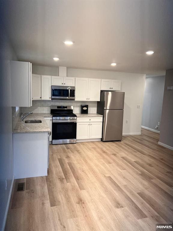 kitchen with white cabinets, stainless steel appliances, light stone countertops, and sink