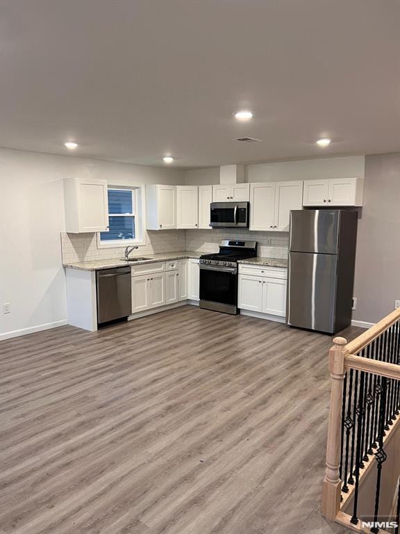 kitchen with light stone countertops, white cabinetry, sink, stainless steel appliances, and light hardwood / wood-style floors