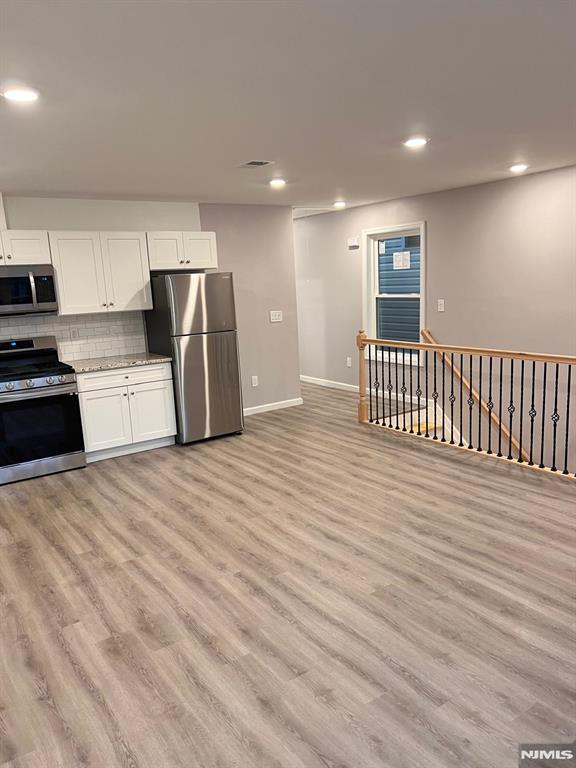 kitchen featuring backsplash, stainless steel appliances, white cabinetry, and light hardwood / wood-style floors