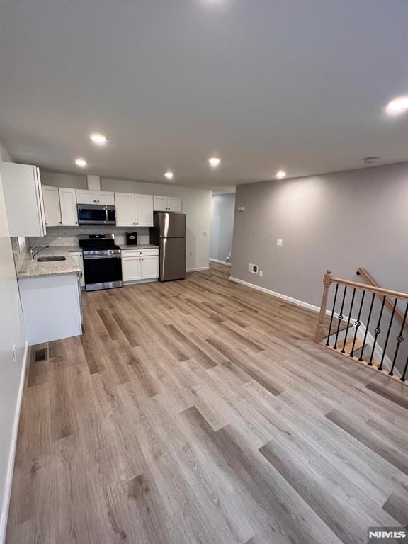 kitchen with sink, light hardwood / wood-style floors, light stone counters, white cabinetry, and stainless steel appliances