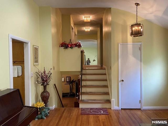 staircase featuring hardwood / wood-style flooring, lofted ceiling, and a notable chandelier