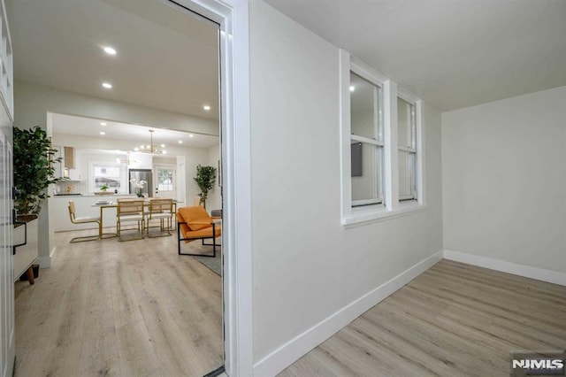 hallway featuring light wood-type flooring and an inviting chandelier